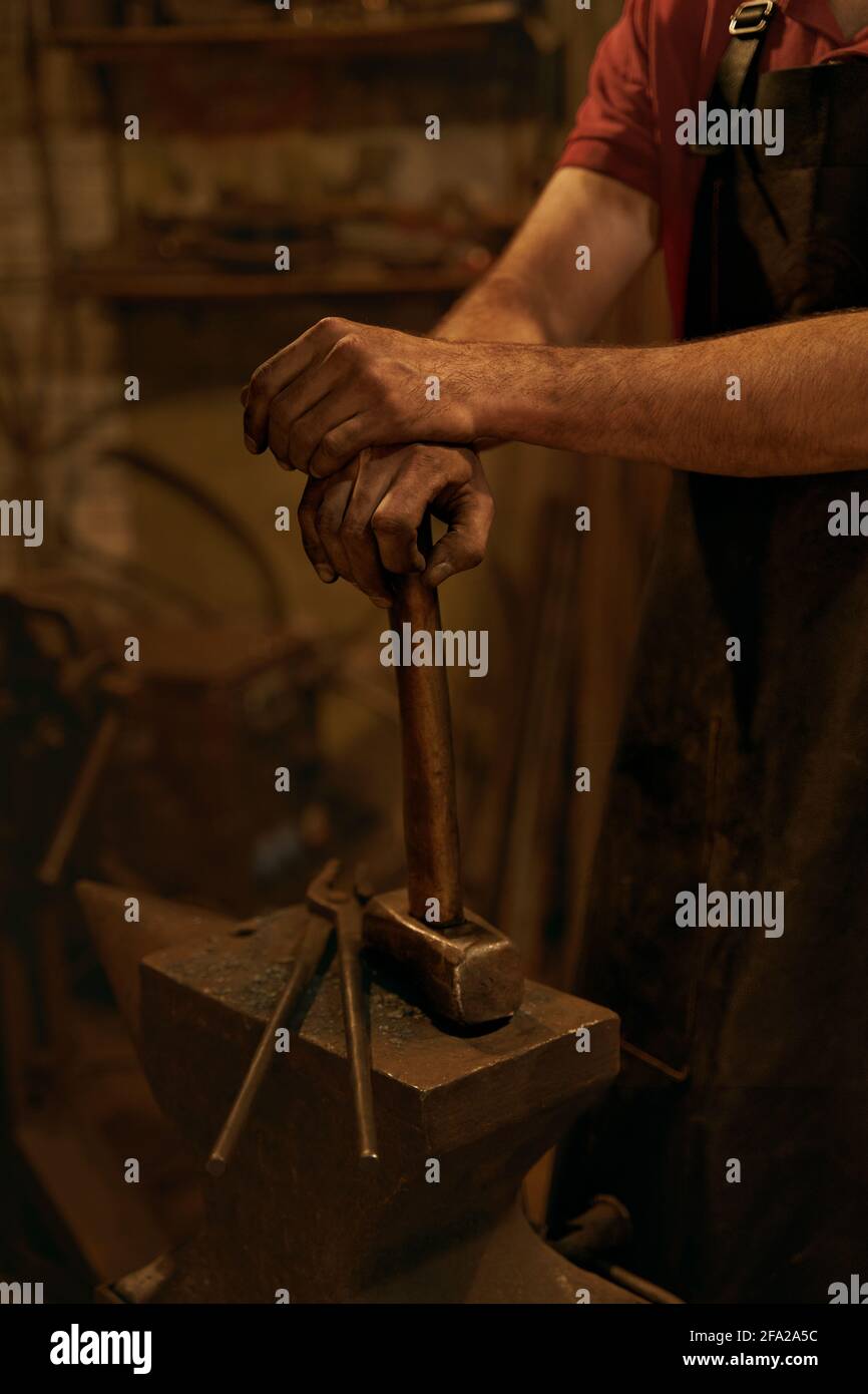 Schmied hält Hammer auf Amboss in der Schmiede Stockfoto