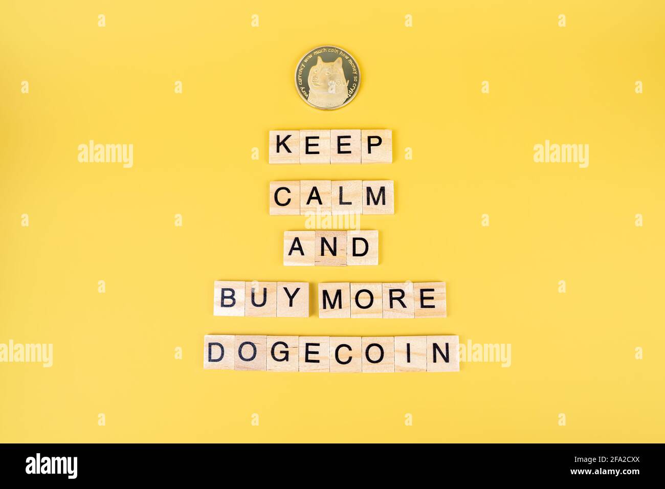Bleiben Sie ruhig und kaufen Sie mehr Dogecoin, lustiges Zeichen über Kryptowährung mit Holzblöcken und Münze mit Hundegesicht auf gelbem Hintergrund. Doge Preisaufstieg kontra Stockfoto