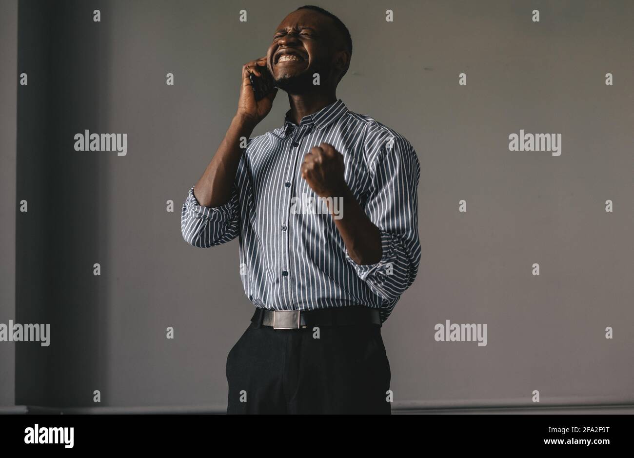 Schwarzer Kerl auf grauem Hintergrund, der am Telefon spricht Happy erfährt die gute Nachricht Stockfoto