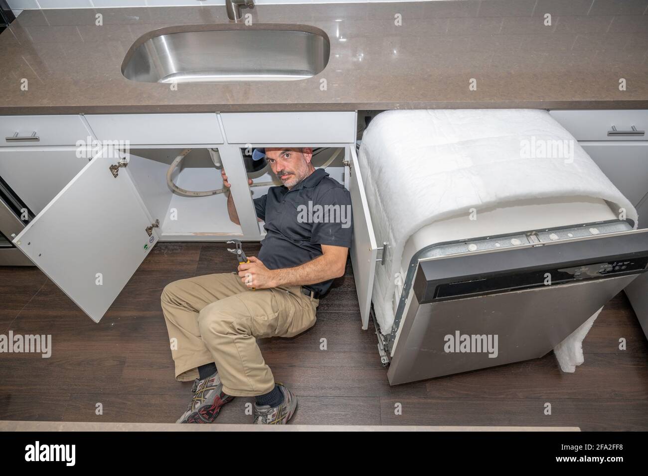 Gerätetechniker unter einem Spülbecken, der an einem Geschirrspüler arbeitet Stockfoto