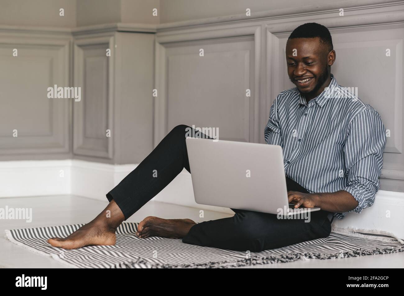 Schwarzer junger Mann, der mit einem Laptop auf dem Boden sitzt Und arbeiten Stockfoto