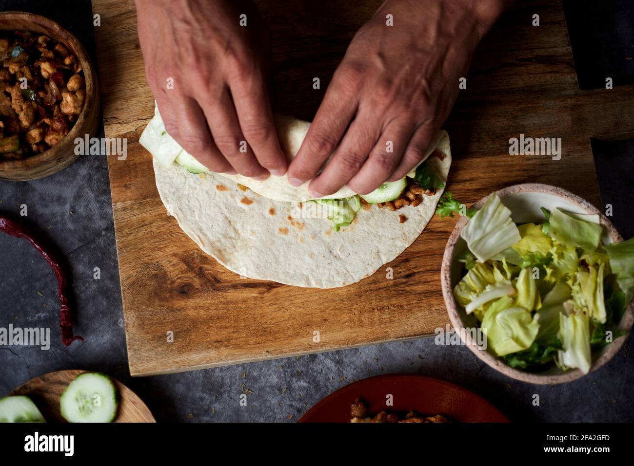 Ein junger Kaukasusmann rollt ein Durum oder einen Burrito, gefüllt mit Hühnerfleisch, das mit Zwiebeln und rotem und grünem Pfeffer gekocht wird, sowie frischem Salat und rohem Salat Stockfoto