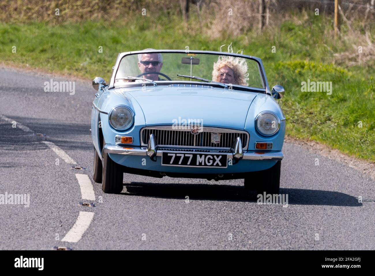 Wind in den Haaren unterwegs, Paar in einem klassischen blauen MGB-Sportwagen, Alresford, Hampshire, Großbritannien Stockfoto