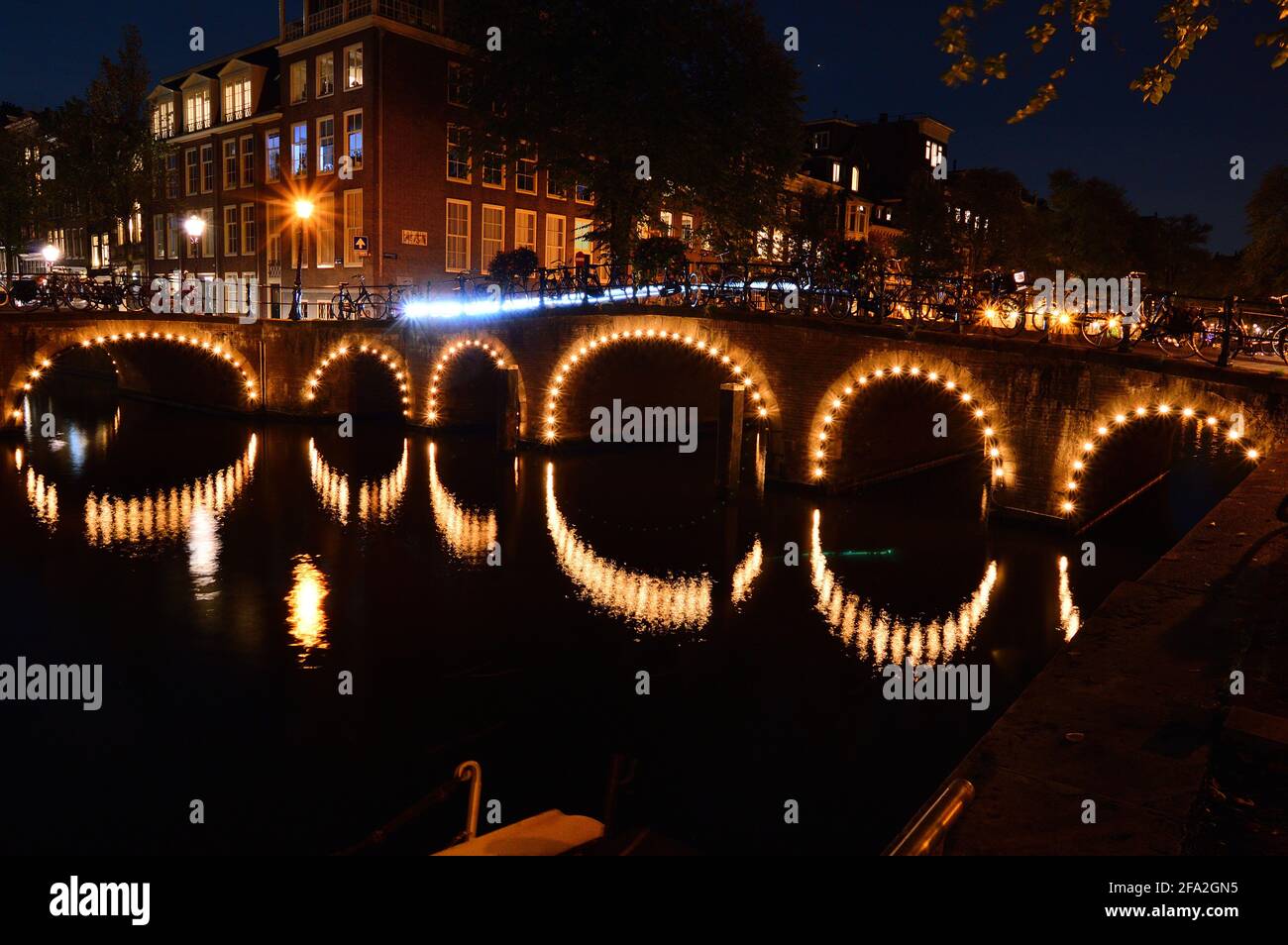 Eine Nacht in Amsterdam. Die beleuchtete Brücke spiegelt sich im Kanalwasser wider. Sommer. Stockfoto