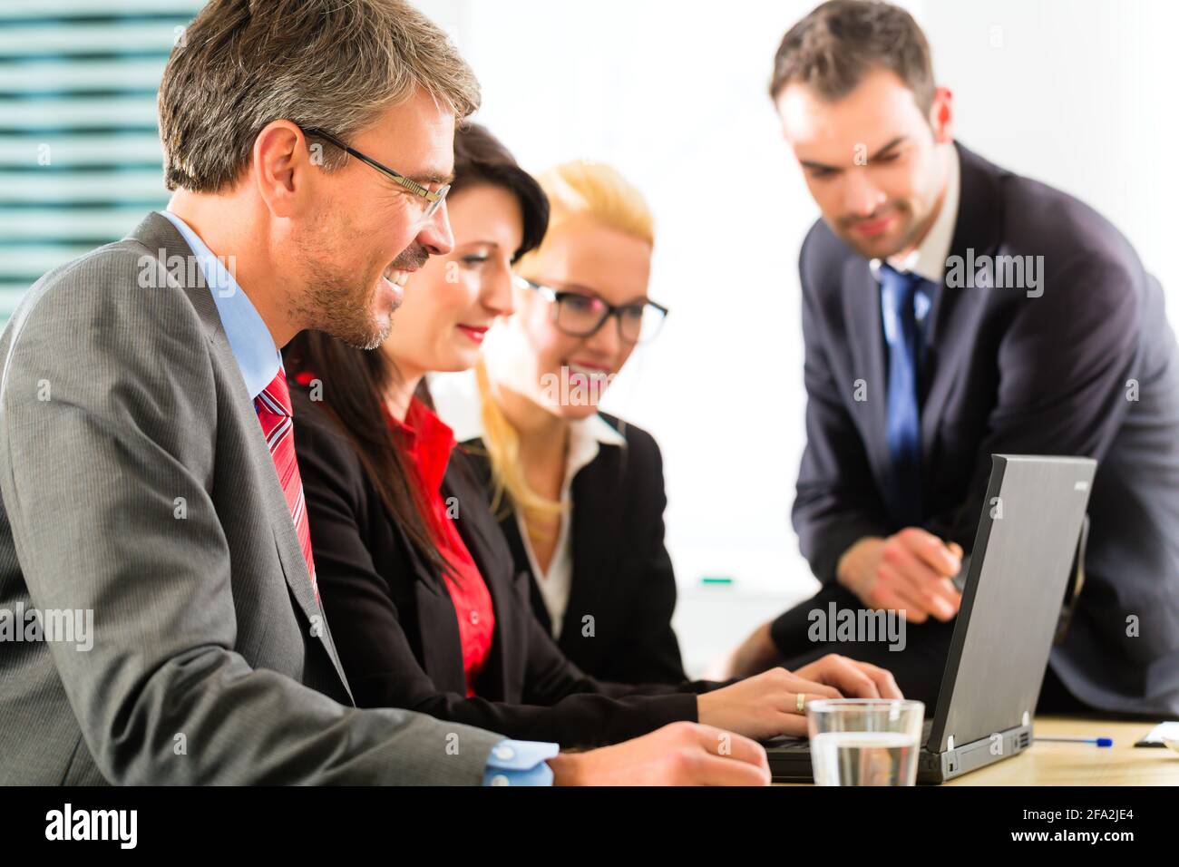 Business - Bildschirm vier Profis im Büro in Geschäftskleidung Blick auf Laptop arbeiten zusammen Stockfoto