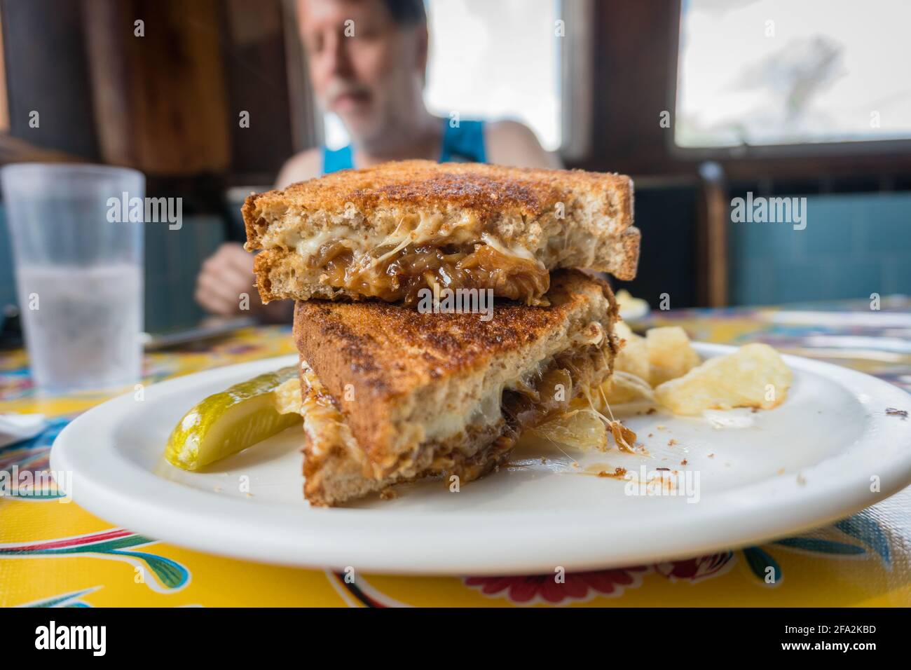 Mann im Hintergrund beim Abendessen mit Nahaufnahme von Delicious Im Vordergrund sieht das gegrillte Käse-Sandwich aus Stockfoto