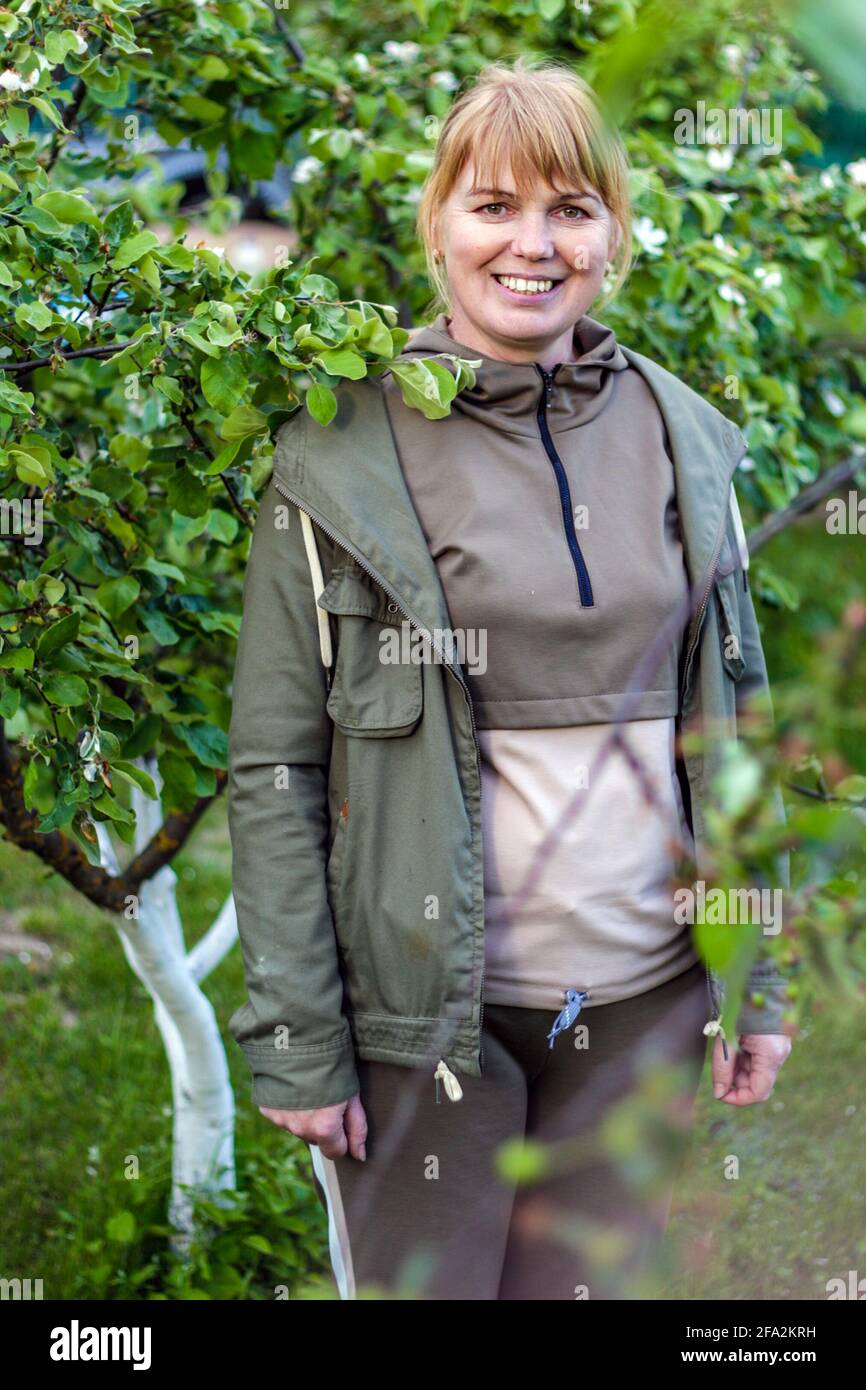 Porträt einer lächelnden, reifen Frau, die im Garten steht. Auf Dem Land. Posiert für die Kamera im Frühlingsgarten. Glück, viel Spaß. Selbstbewusst, kaukasisch Stockfoto