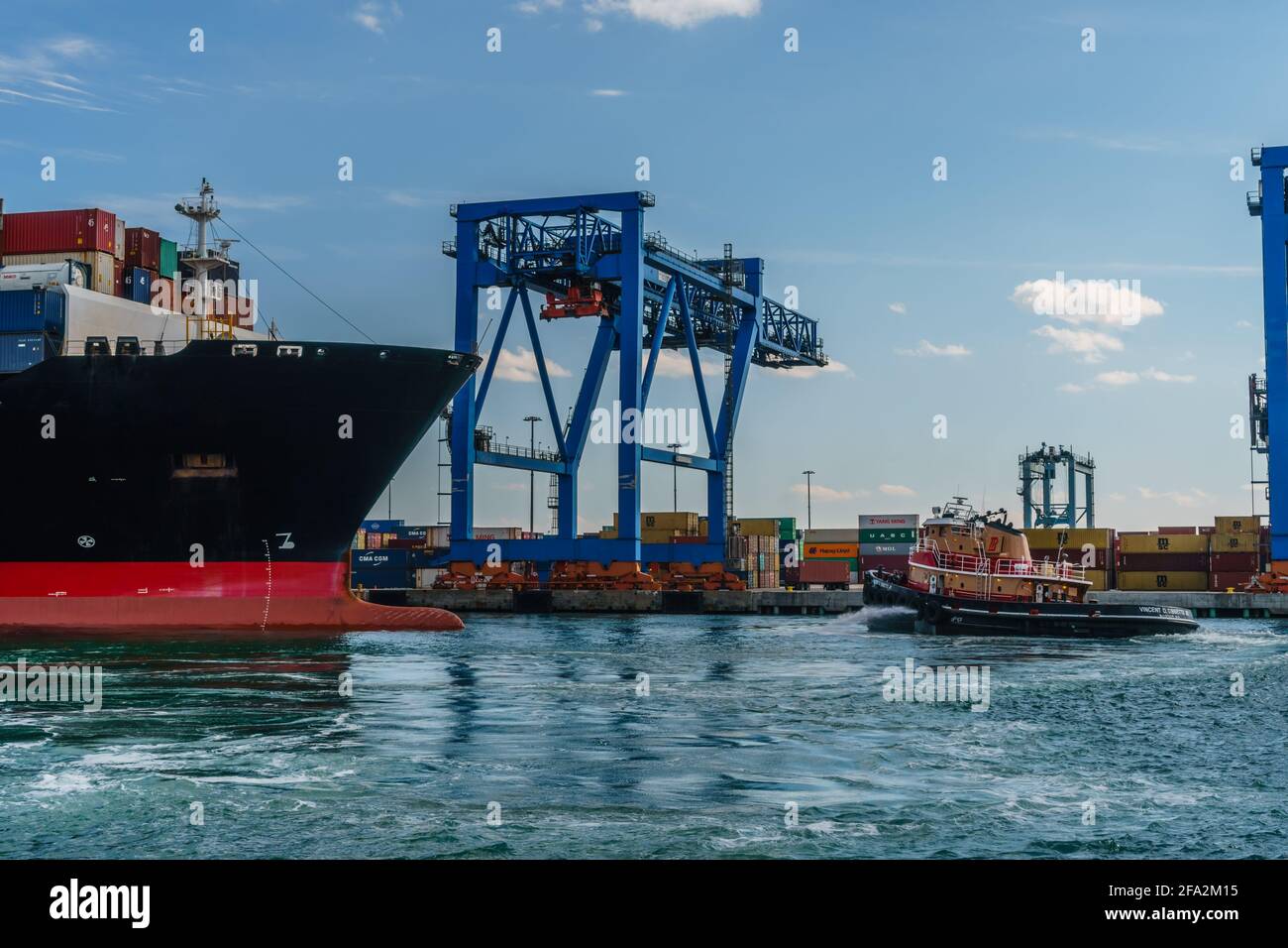 Boston, MA, USA - 11. März 2019: Voll beladenes Containerschiff verlässt den Hafen von Boston mit Schlepper und Schiffskräne im Hintergrund. Stockfoto