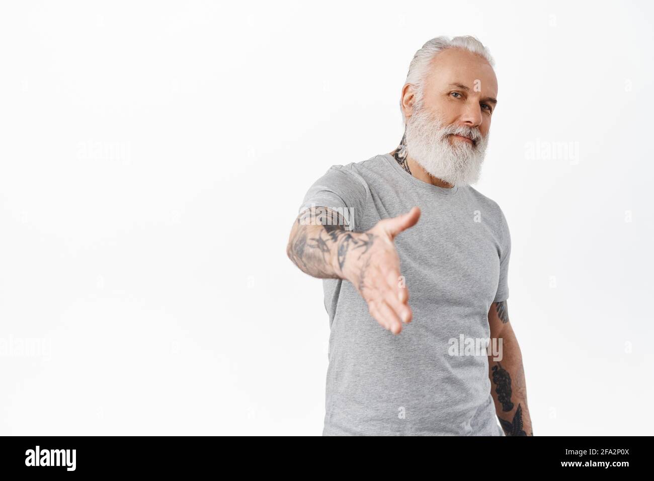 Stilvoller und selbstbewusster älterer Mann mit Tattoos streckt die Hand zum Händeschütteln aus, grüßt jemanden, grüßt ihn, torpediert sich mit festem Gruß, steht Stockfoto