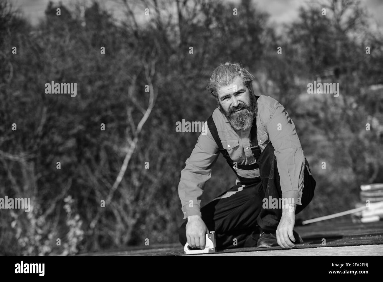 Dachmontage. Bärtiger Mann arbeitet im Freien. Dachmechanik Konzept. Reparatur überprüfen und austauschen. Provisorische Ausrüstung oder Strukturen montieren. Strukturell Stockfoto