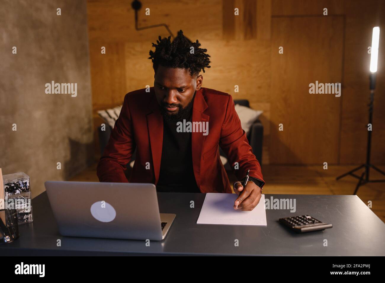Schöner schwarzer afroamerikanischer Mann, der am Laptop-Computer arbeitet, während er hinter dem Schreibtisch im gemütlichen Wohnzimmer sitzt. Freiberuflicher Mitarbeiter, Der Von Zu Hause Aus Arbeitet Stockfoto