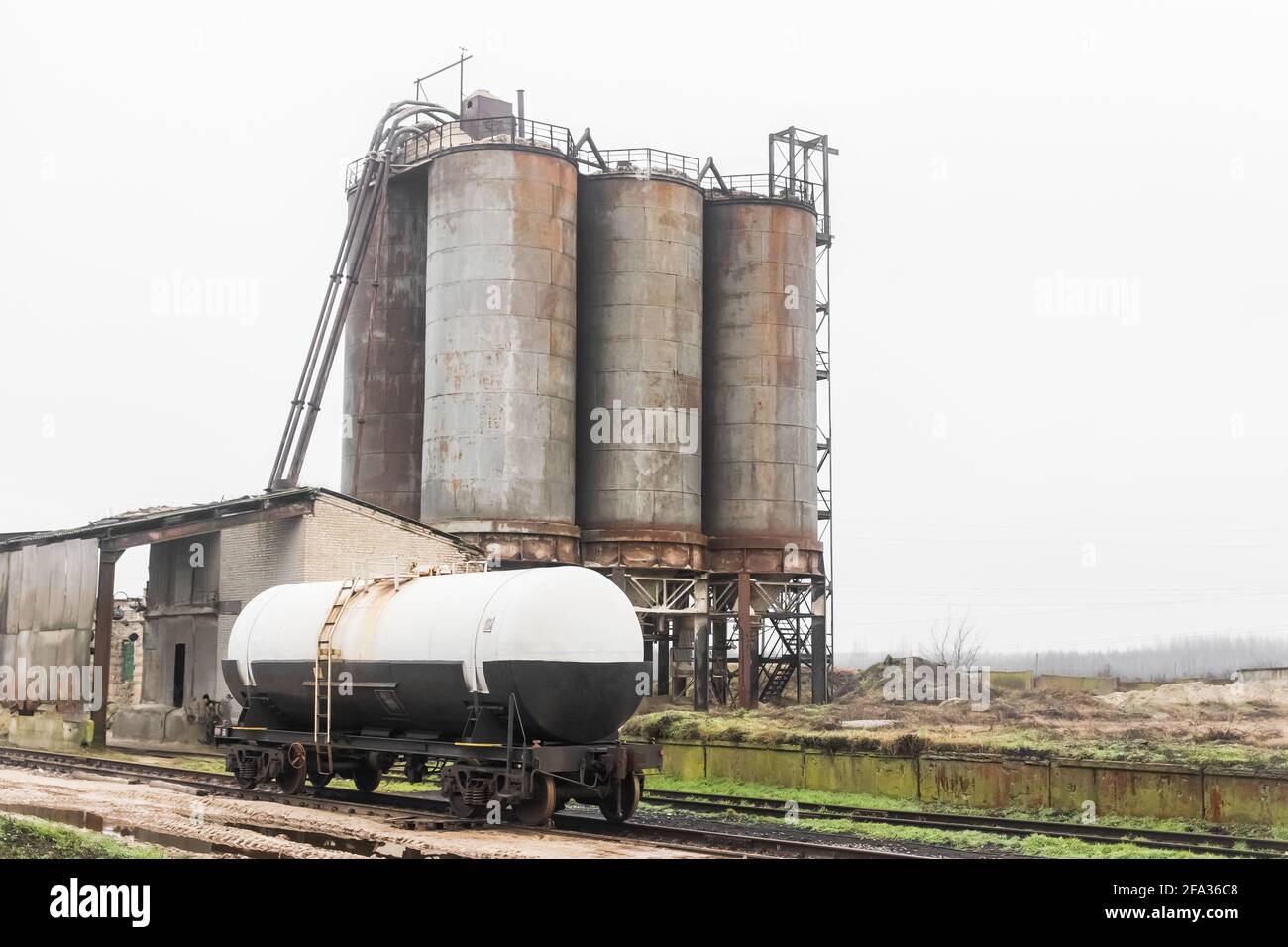 Düngertank auf den Schienen des Eisenbahnindustriebahnhofs vor dem Hintergrund alter Sandlagertanks in einer verlassenen Anlage. Stockfoto