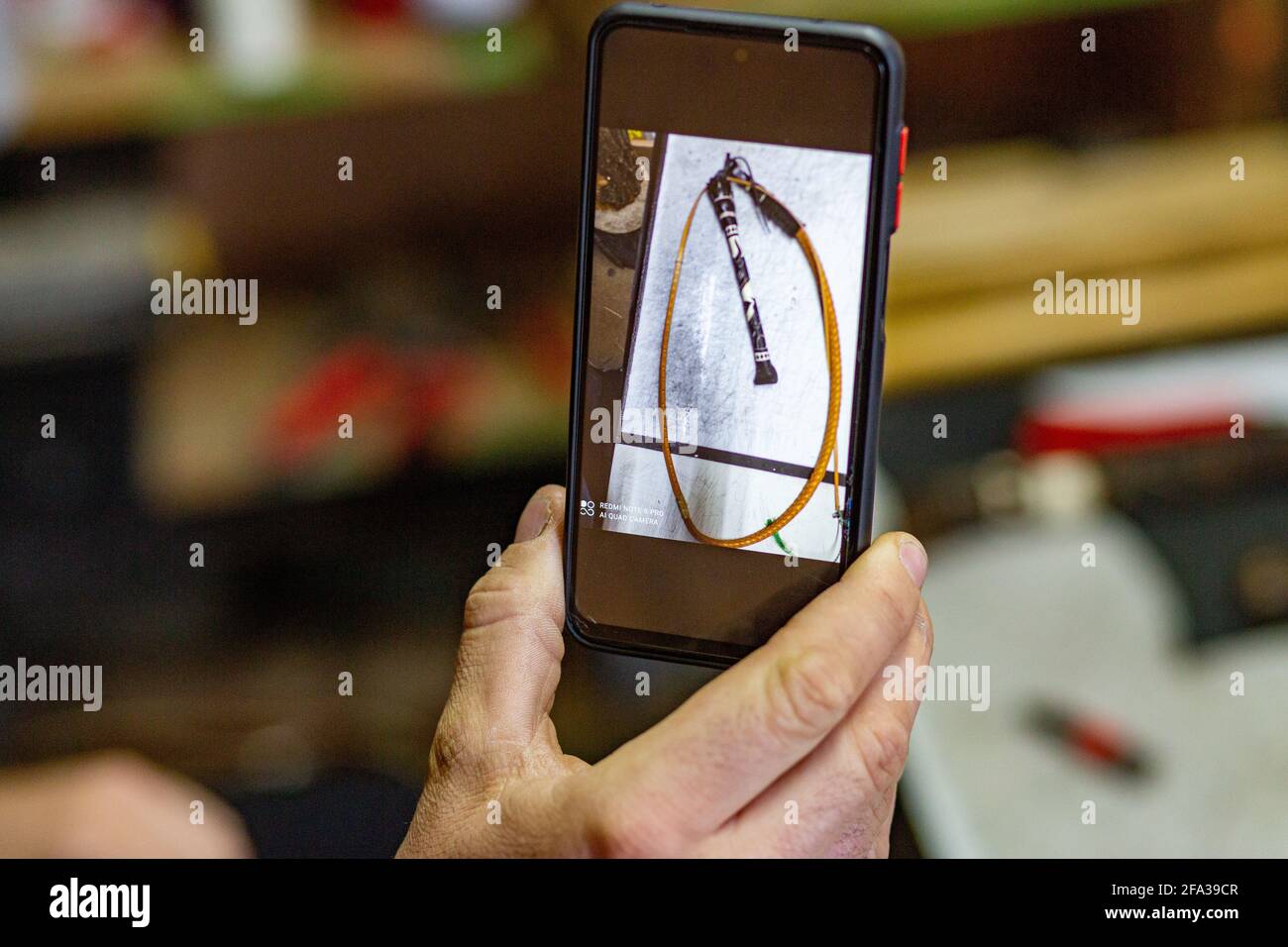 Der Mann zeigt ein Foto einer handgefertigten traditionellen Schäferpeitsche, die er auf seinem Telefon gemacht hat. Stockfoto