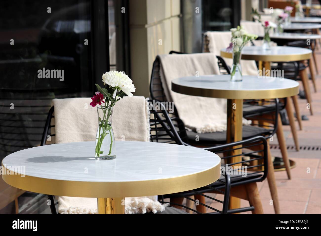 Straßencafé mit leeren Tischen im Freien, Stadt während der Coronavirus-Pandemie. Blumenvasen auf Tischen und Vintage-Holzstühle mit warmen Karos Stockfoto
