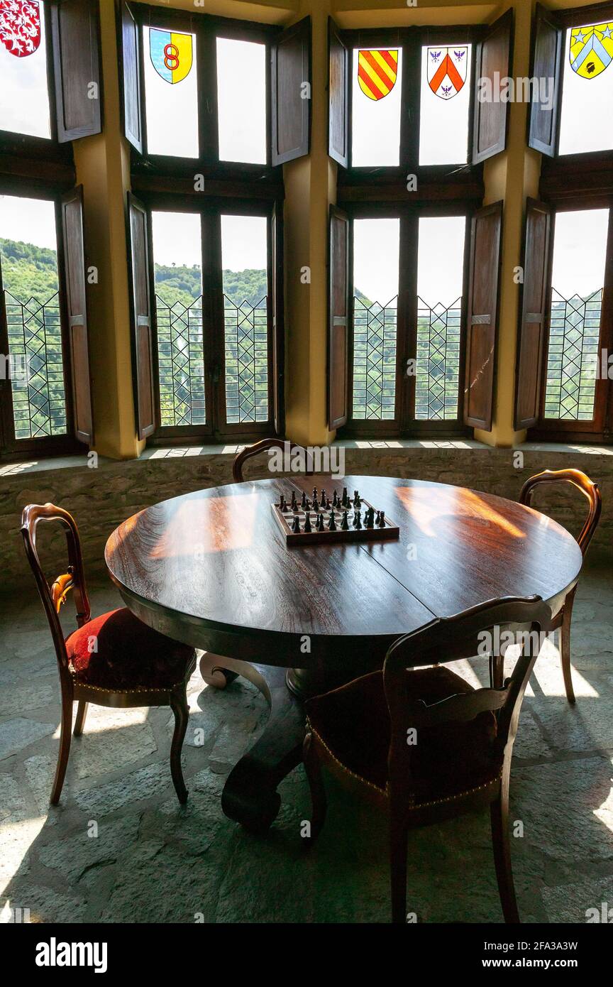 Zimmer des Château de Chouvigny. Runder Tisch mit Schachbrett vor dekorativen Glasfenstern mit edlen Wappen. Chouvigny, Frankreich, europa Stockfoto