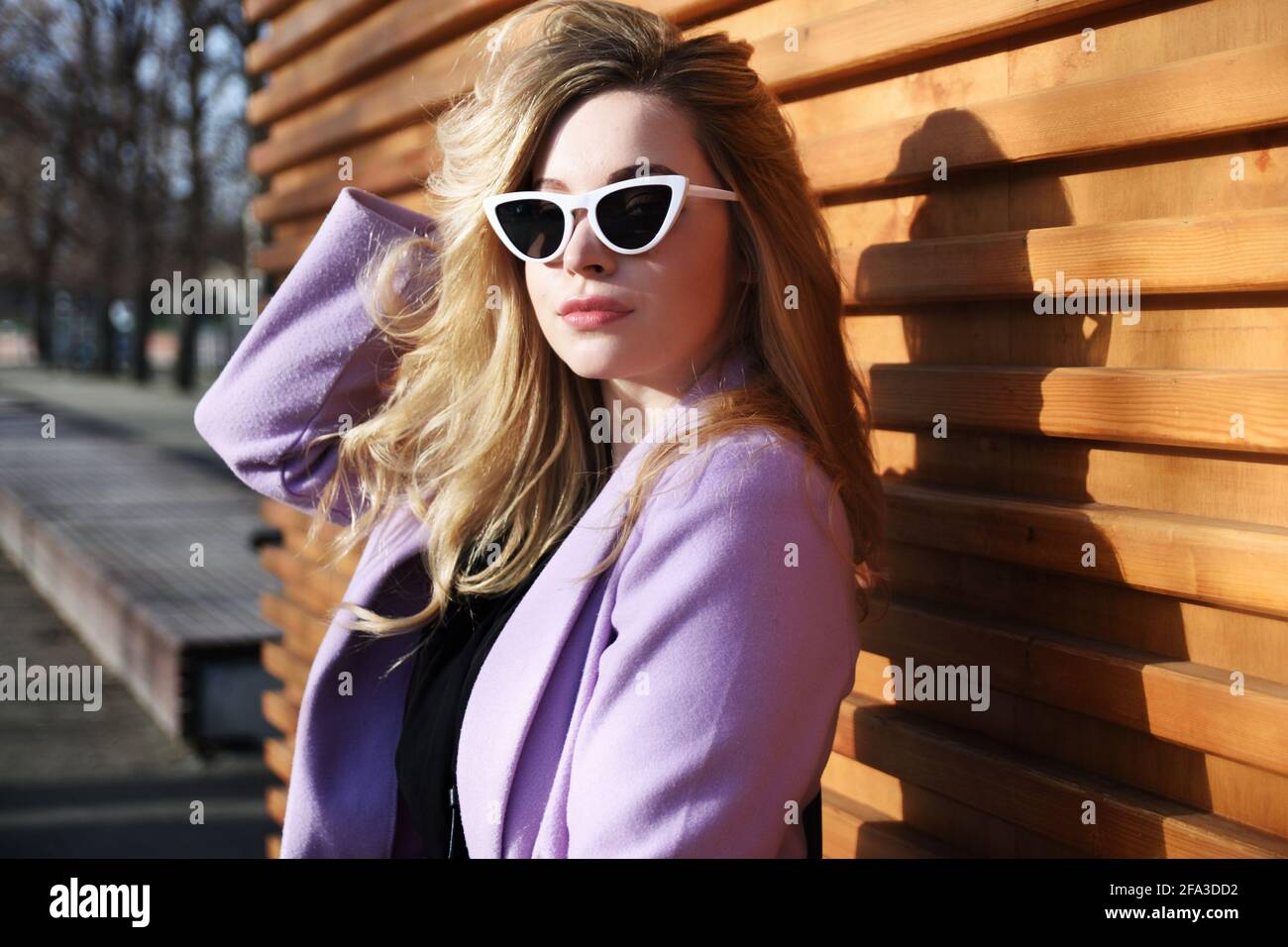 Junge Frau in Breslau. Studentin mit blonden Haaren, violettem Mantel und Sonnenbrille. Stockfoto