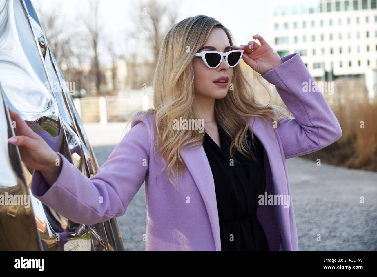 Junge Frau in Breslau. Studentin mit blonden Haaren, violettem Mantel und Sonnenbrille. Stockfoto