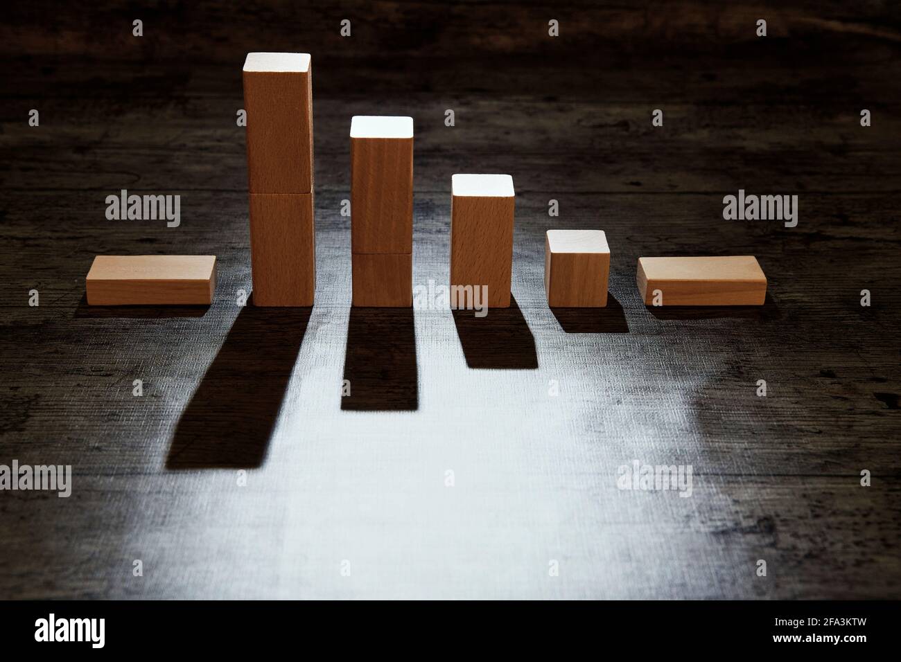 Satz von Holzblöcken in Form eines schwächenden Diagramms, das die Abnahme zeigt. Low-Key-Fotografie mit harten Schatten. Konzept des Rückgangs, sinkender Bestand Stockfoto