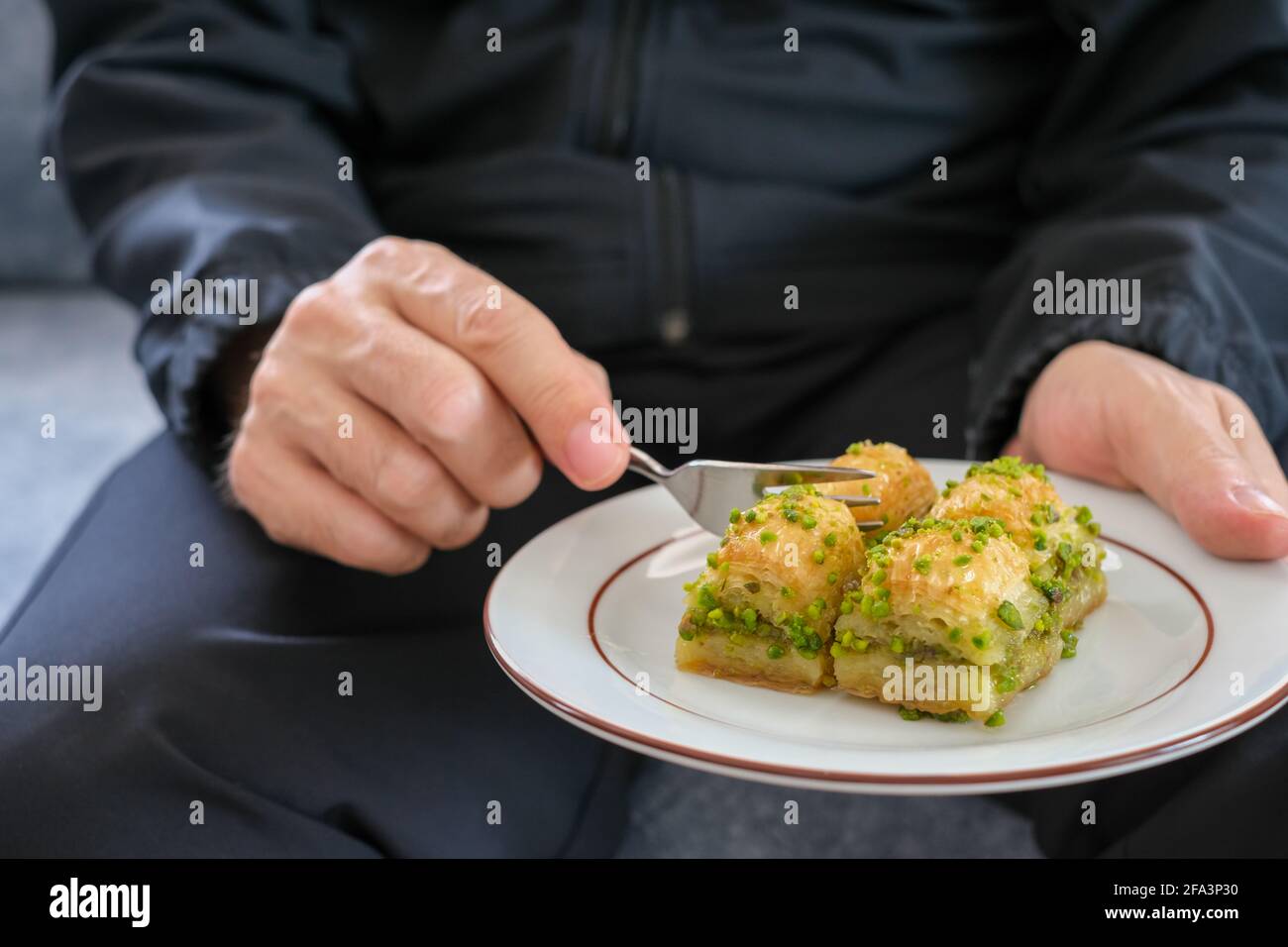 Der Mann hält in einem Teller Baklava und er Isst türkisches Baklava ...