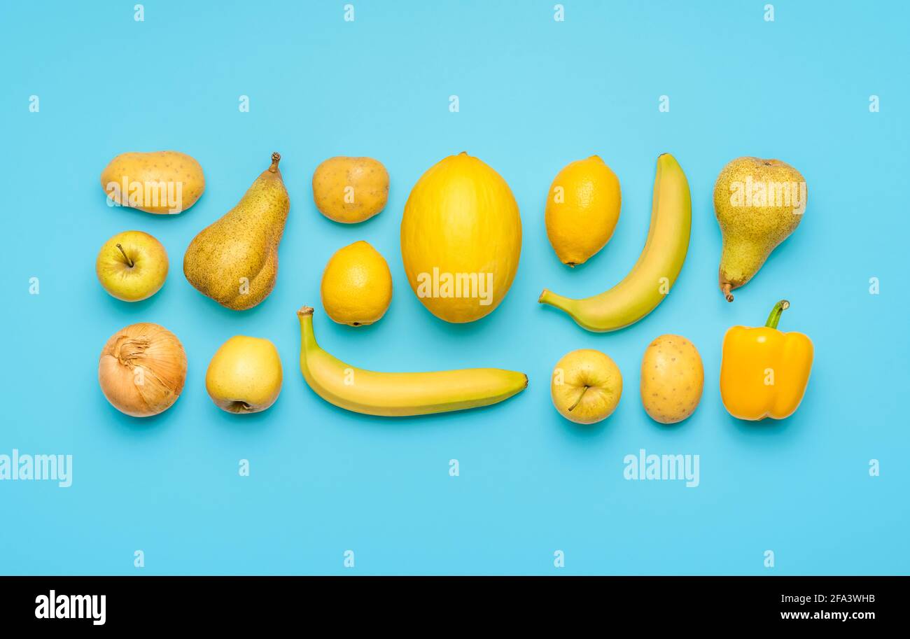 Flach mit verschiedenen gelben Früchten und Gemüse auf einem blauen Tisch legen. Frisches Gemüse und Obst symmetrisch auf farbigem Hintergrund angeordnet Stockfoto