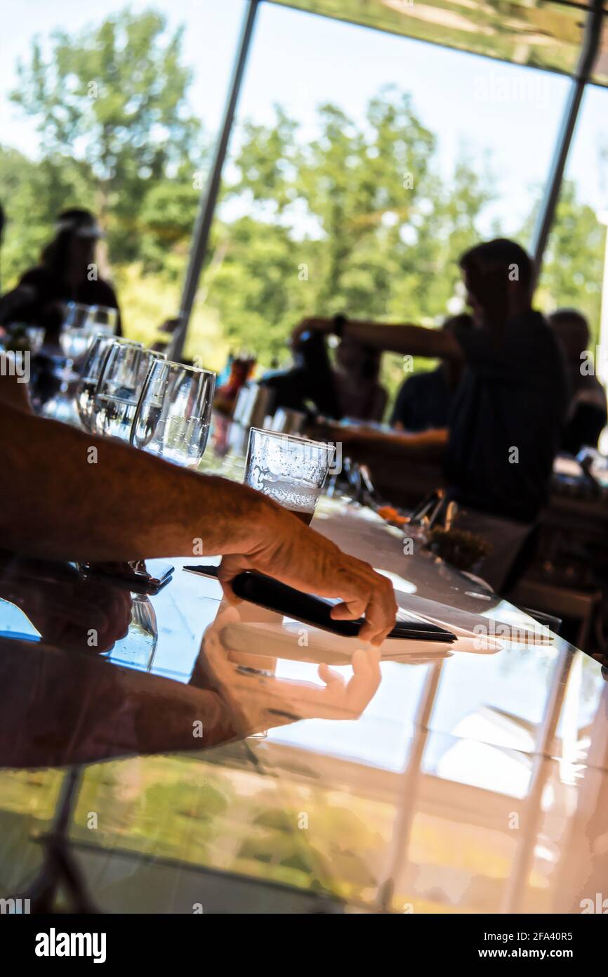 Zahlung des Schecks - beschnittene mans Arm und Hand Picks Oben Ordner mit Check von reflektierenden Bar Top mit Silhouetten Server und Kunden in der Ferne Stockfoto