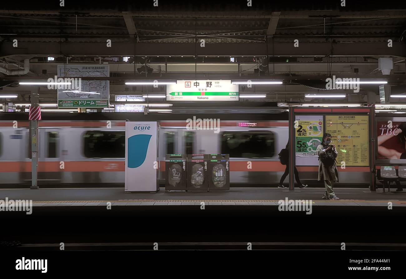 Tokio, Japan - 20 2020. Oktober: Nachtansicht einer Plattform am Bahnhof Nakano, mit einem fahrenden Zug und ein paar Pendlern sichtbar Stockfoto