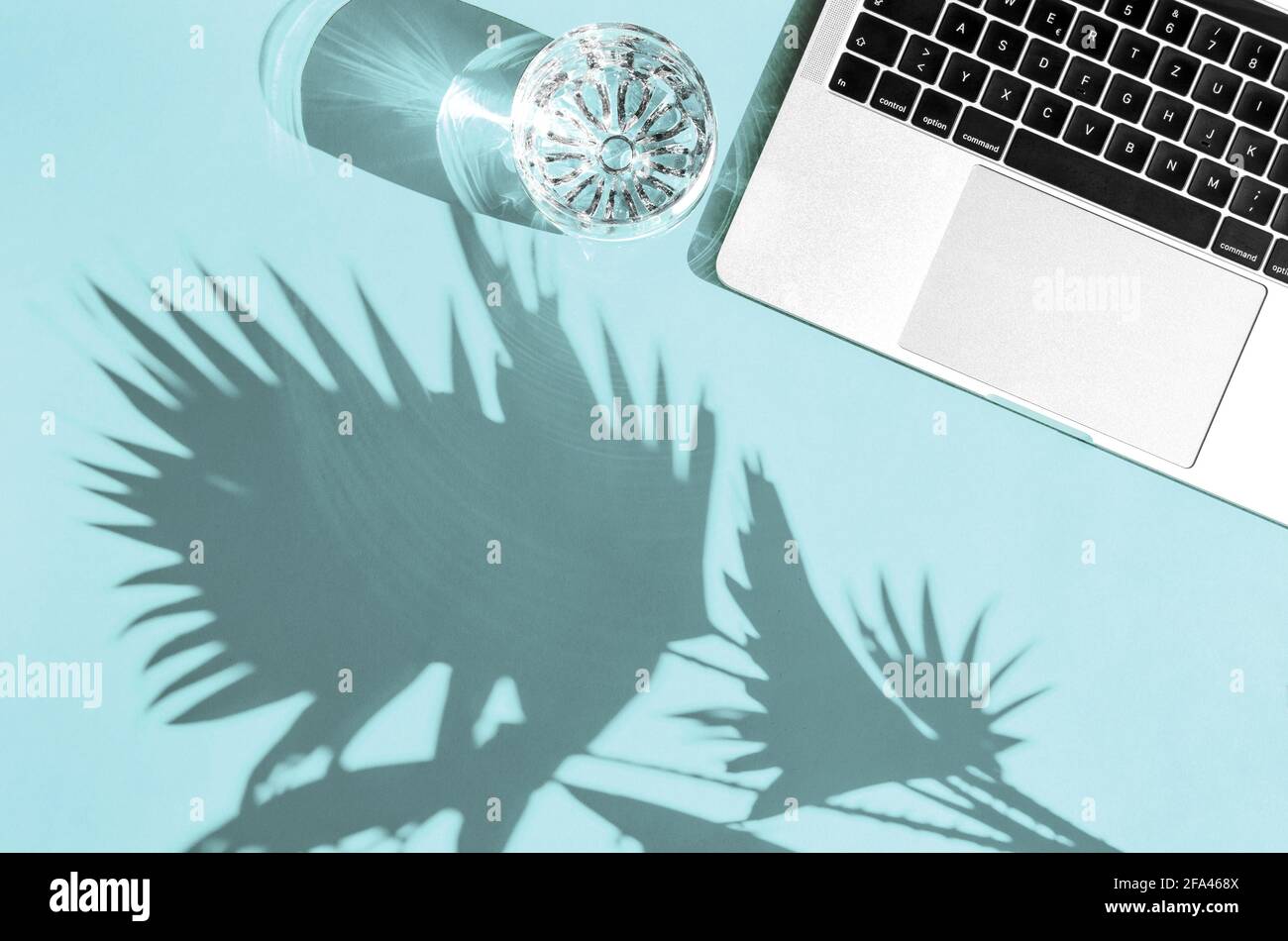 Laptop und Glaswasser mit Sonnenschatten. Home Office Arbeitsplatz flach legen Stockfoto