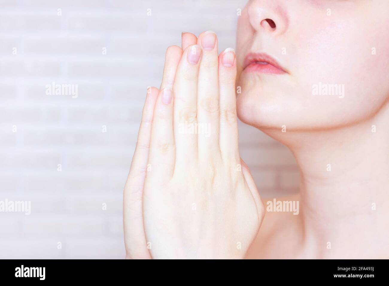 Die junge kaukasische Frau betet Gott und bittet mit den Händen in der Nähe ihres Gesichts um Hilfe. Stockfoto