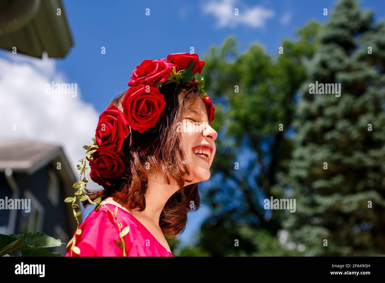 Ein lachendes kleines Mädchen mit geschlossenen Augen trägt eine Krone Von Rosen Stockfoto