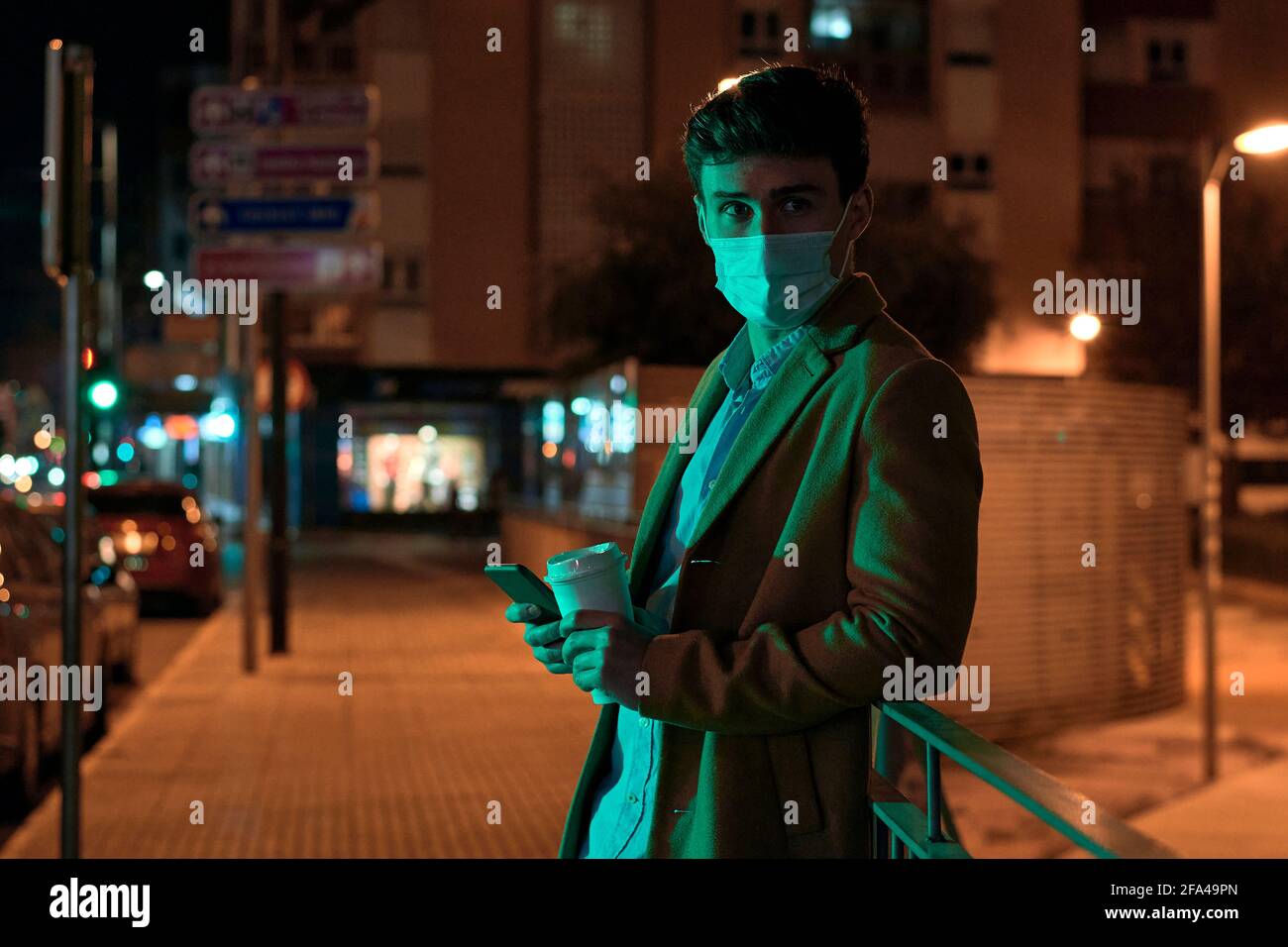 Junger Geschäftsmann mit einer Gesichtsmaske, die von den Lichtern der Stadt beleuchtet wird Nachts Stockfoto