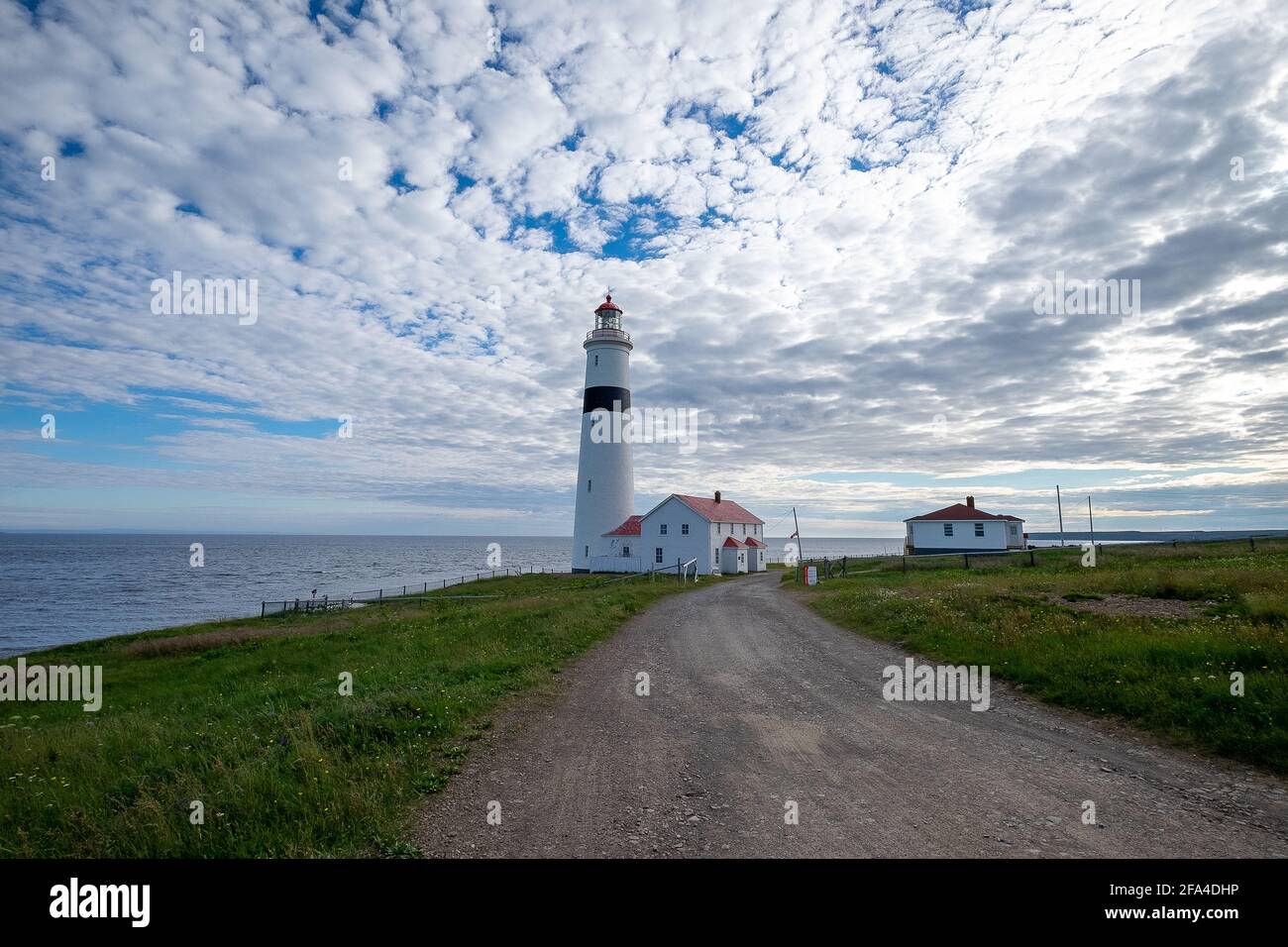 Point Amour Historic Lighthouse am Rande des Atlantischen Ozeans. Der blaue Himmel wird von flauschigen Wolken verdeckt. Stockfoto