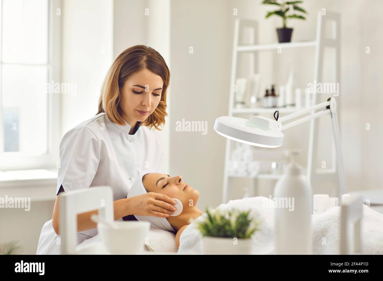 Junge Kosmetikerin oder Dermatologin, die das Gesicht der Frau mit Baumwolle reinigt Pads im Spa-Salon Stockfoto