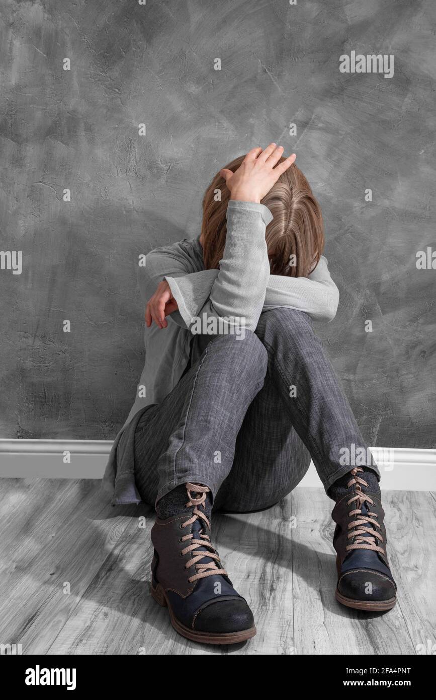 Eine Frau, die an einer Wand sitzt, hält ihren Kopf fest Ein Zustand der Depression oder ein großes Problem Stockfoto