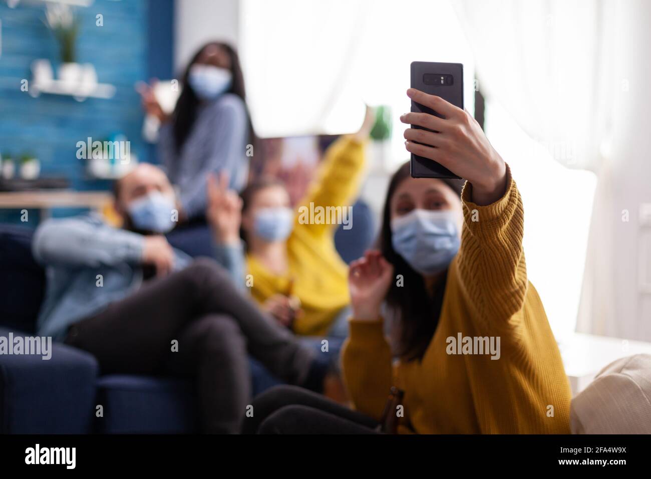 Multirassische Freunde, die Selfie mit Gesichtsmasken während covid 19 Ausbruch, neue normale Lifestyle-Konzept mit Menschen Spaß im Wohnzimmer unter Beachtung der sozialen Distanz, um die Ausbreitung von Viren zu verhindern Stockfoto