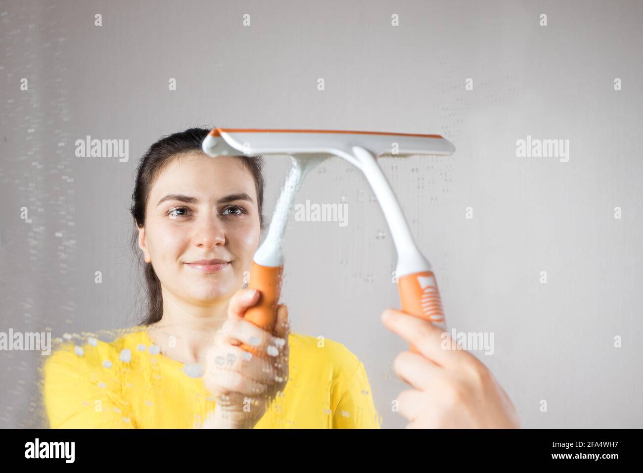 Die Putzfrau reinigt den Spiegel mit einem Wasserspender und Fensterreiniger. Hausreinigung. Reinigungsservice Stockfoto