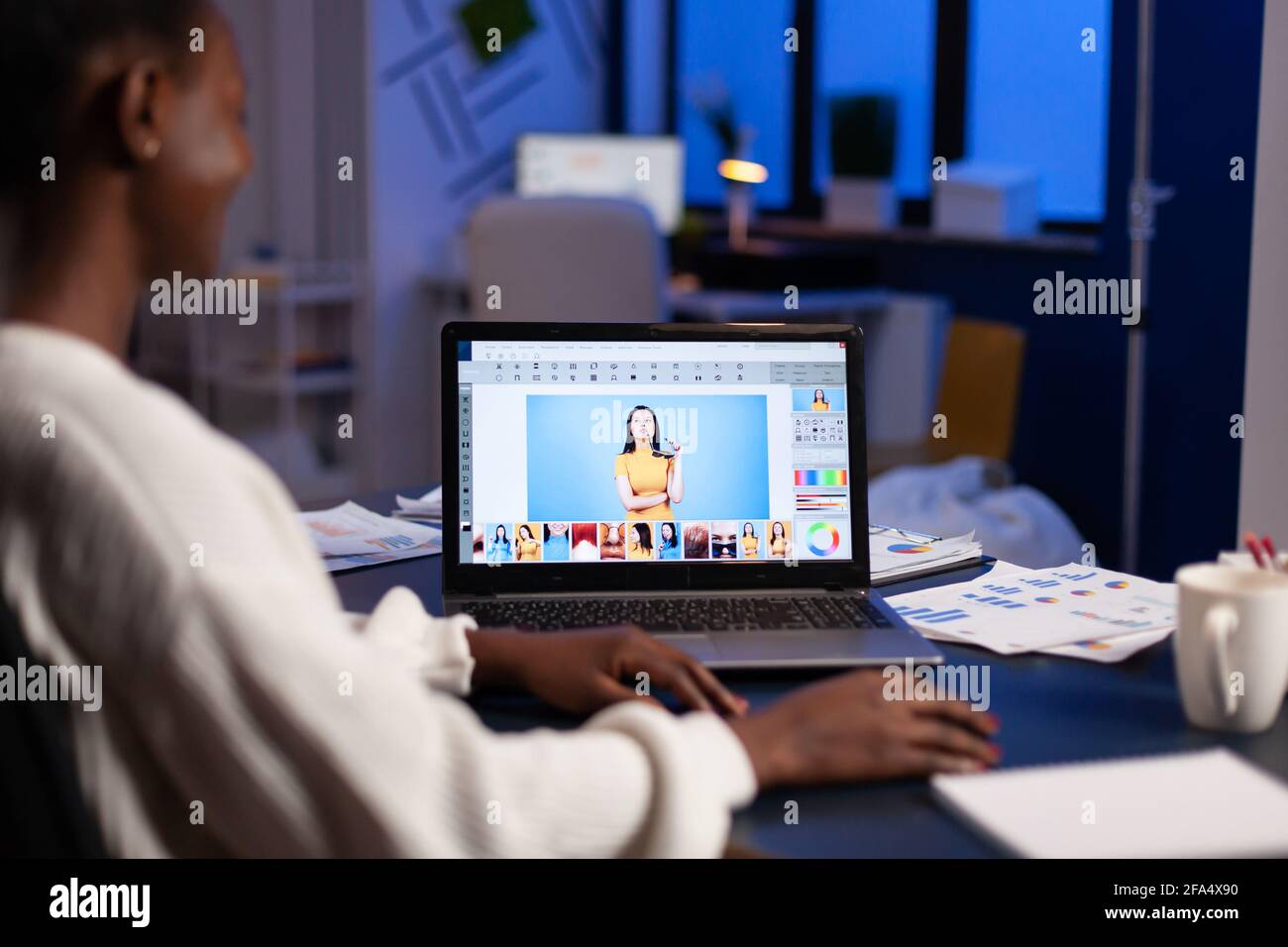 Dunkelhäutiger Freiberufler Retuscherin Frau, die Überstunden am Laptop mit Fotobearbeitungssoftware arbeitet. Professioneller Grafikeditor Retusche Foto eines Kunden in der Nacht im Home Office auf Performance-pc. Stockfoto
