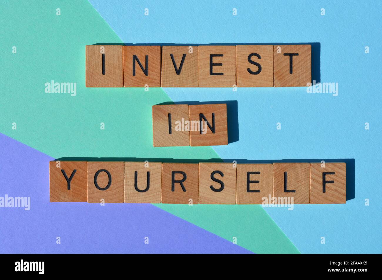 Investieren Sie in sich selbst. Motivierende Wörter in hölzernen Buchstaben, isoliert auf buntem Hintergrund Stockfoto