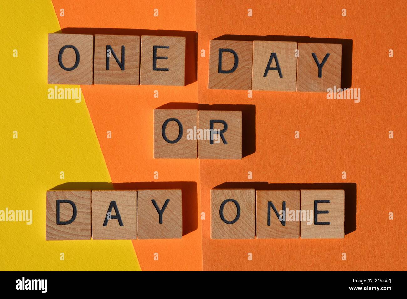 „One Day“ oder „Day One“, Motivationswörter in Holzbuchstaben, isoliert auf gelbem und orangefarbenem Hintergrund Stockfoto