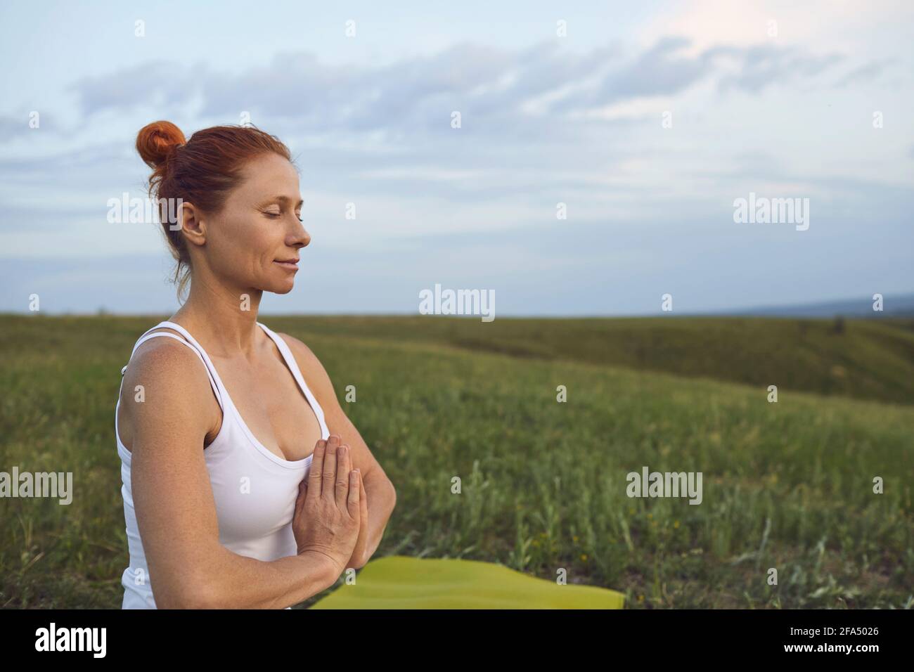 Entspannte reife Frau, die Meditation auf einer ruhigen grünen Wiese versucht Um innere Harmonie zu erreichen Stockfoto