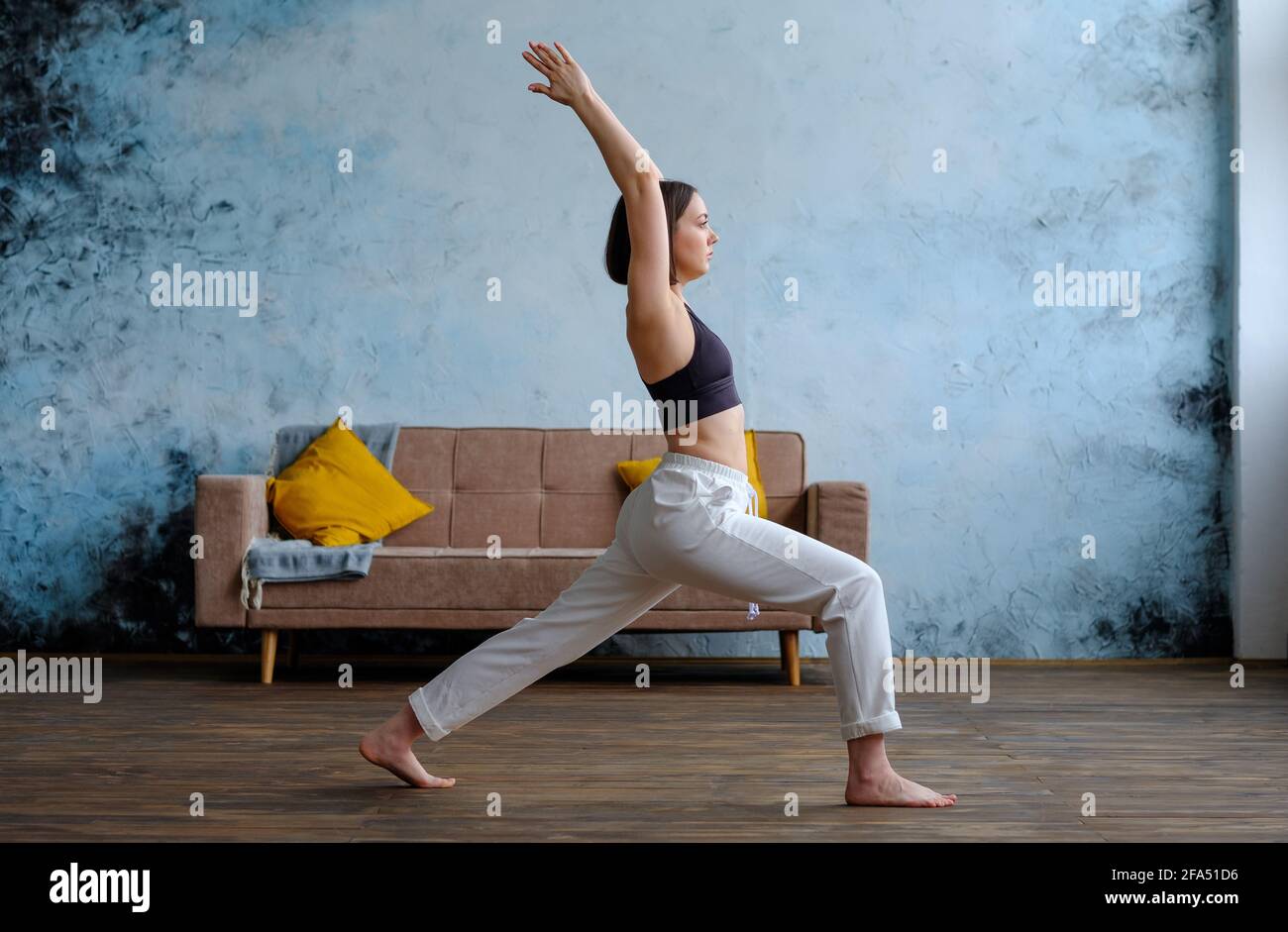 Frau in ihrem Wohnzimmer in Krieger-Yoga-Pose. Stockfoto