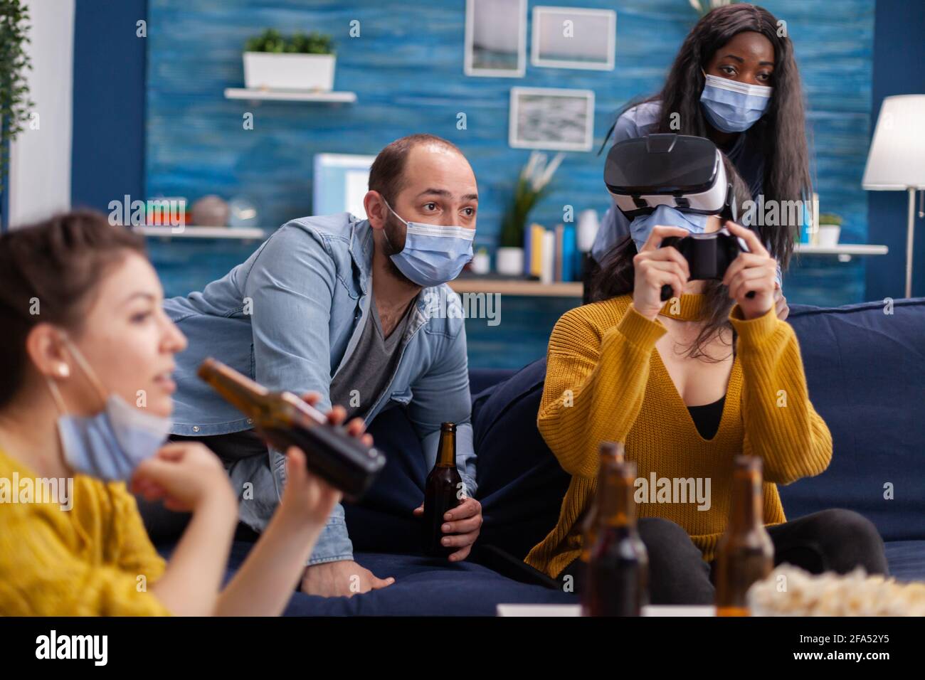 Gemischt raste Freunde im Wohnzimmer mit einem Videospiel competion halten soziale Distanzierung tragen Gesichtsmaske, um Krankheit mit covid zu verhindern. Erleben Sie virtuelle Realität. Konzeptuelles Image. Stockfoto