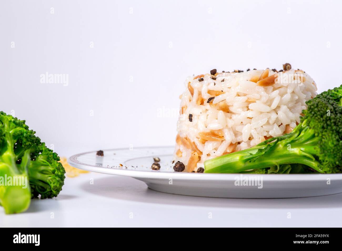 Reis mit Gerstennudeln und frischem Brokkoli auf dem Teller. Stockfoto