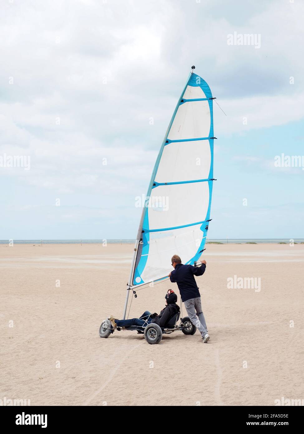 Sand Yacht Land Segeln am Strand Plage de Ouistreham in Frankreich. Ein Mann, der einer Yacht auf dem Sand hilft Stockfoto