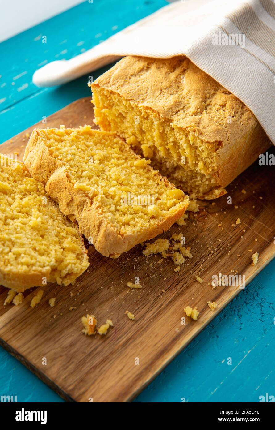 Maisbrot ist Brot mit Maismehl, Maismehl. Schöner hausgemachter, gelber Maisbrot-Laib unter einem Baumwolltuch. Blauer Holzhintergrund. Stockfoto