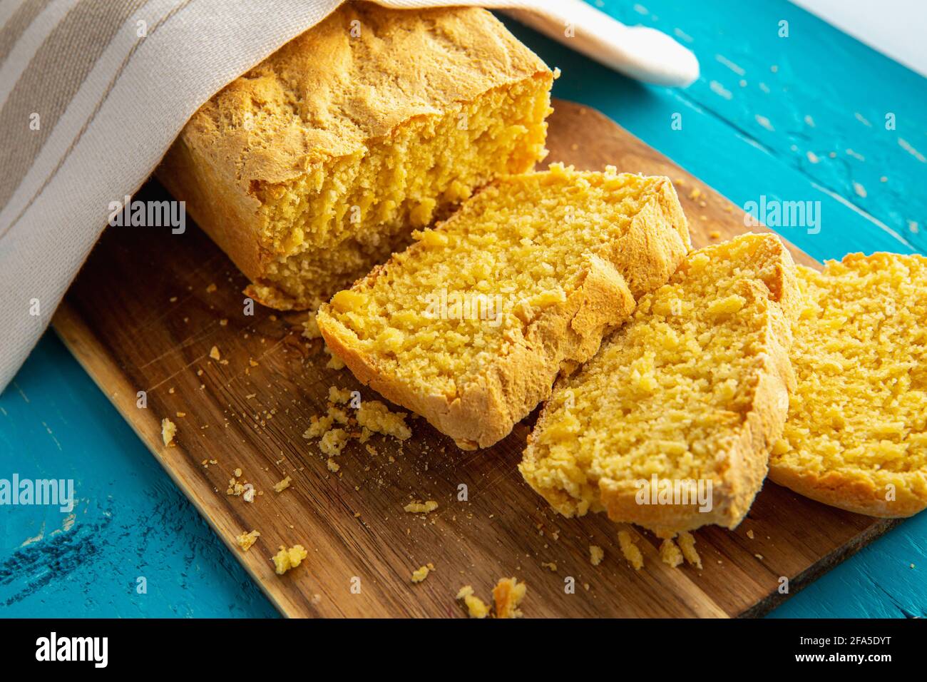 Maisbrot ist Brot mit Maismehl, Maismehl. Schöner hausgemachter, gelber Maisbrot-Laib unter einem Baumwolltuch. Blauer Holzhintergrund. Stockfoto