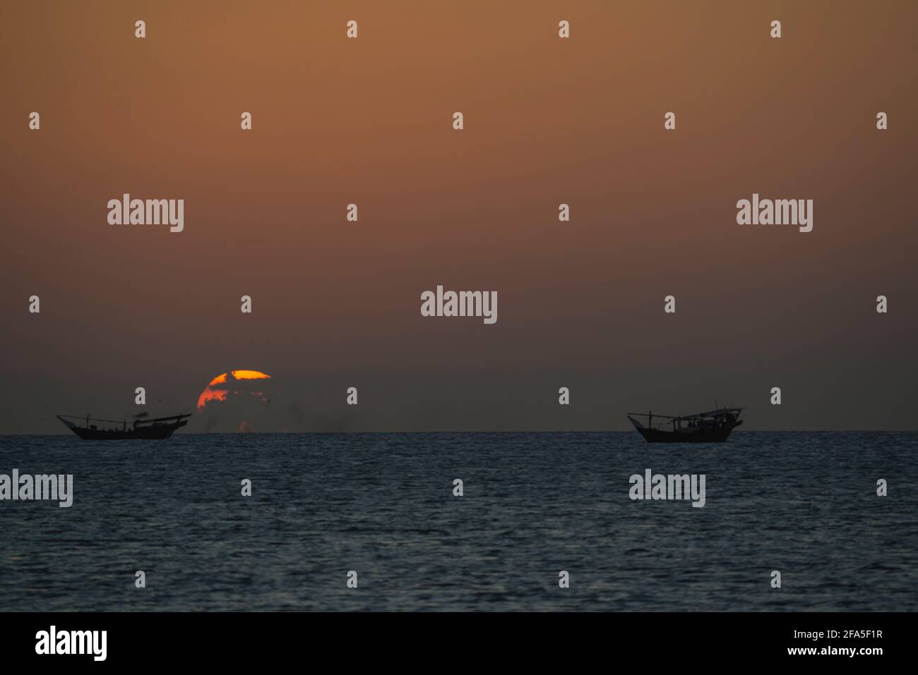 Sonnenuntergang am Arabischen Meer mit Daus, die auf dem Wasser schwimmen, von der Südspitze der Insel Masirah, Oman aus gesehen Stockfoto