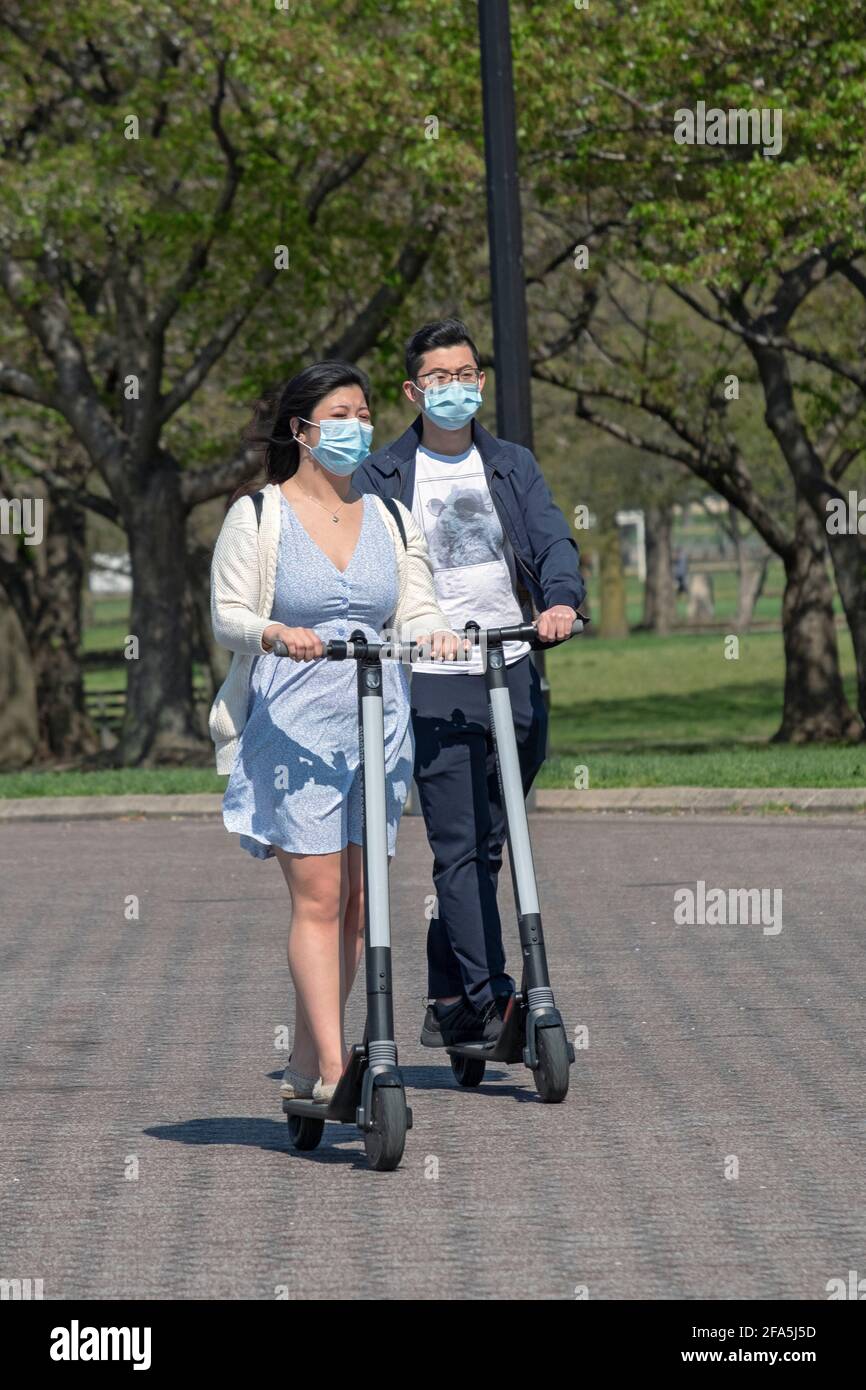 Ein asiatisch-amerikanisches Paar fährt eng zusammen auf motorisierten Motorroller. Im Flushing Meadows Corona Park in Queens, New York City. Stockfoto