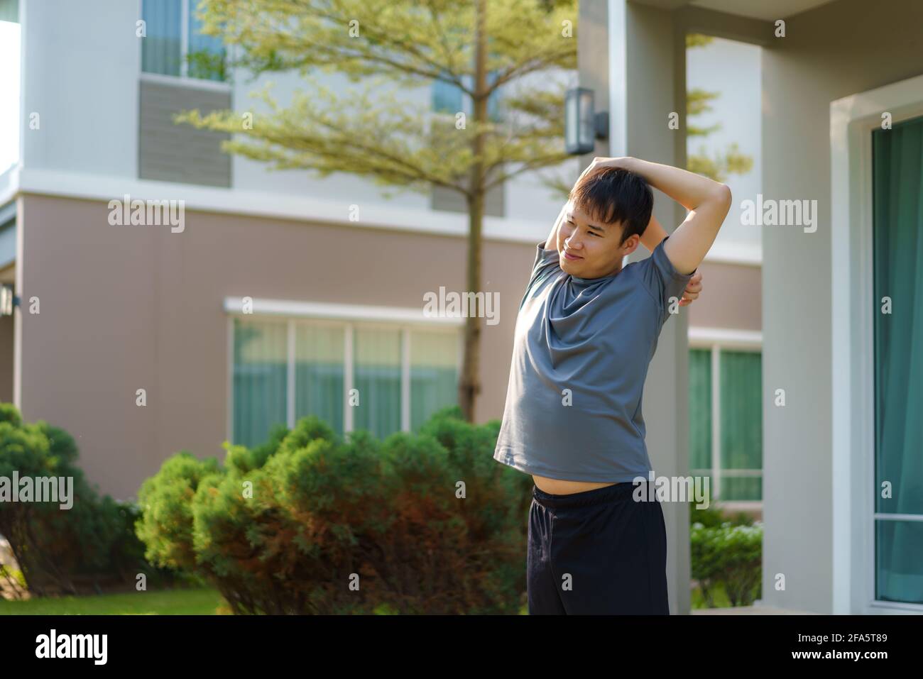 Ein asiatischer Mann, der sich vor oder nach dem Training vor der Haustür in der Nachbarschaft zum Aufwärmen oder Abkühlen ausdehnt, um täglich Gesundheit und Wohlbefinden zu erhalten Stockfoto