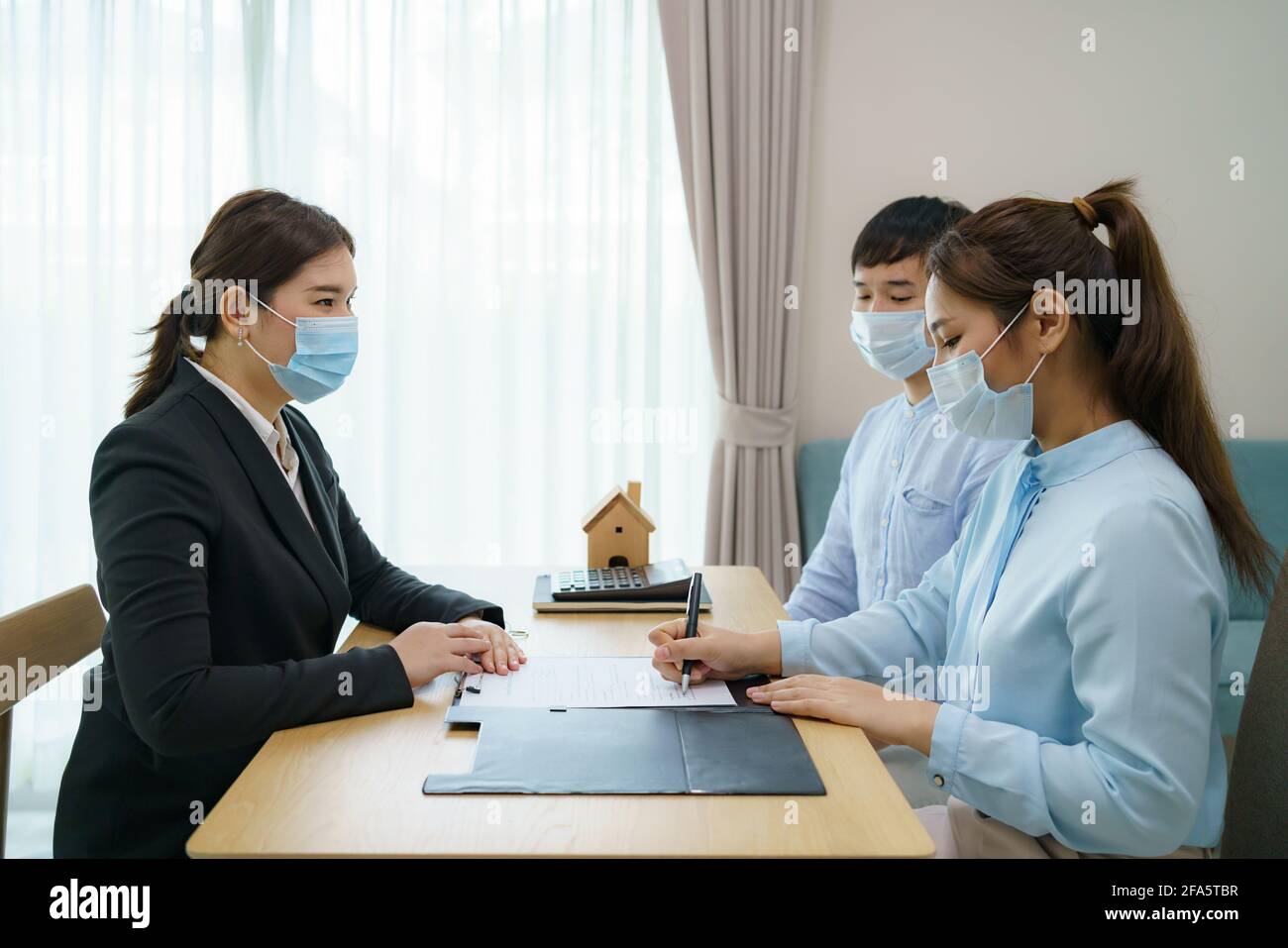 Die Immobilienmakler asiatischer Frauen lassen Kunden Verträge zum Verkauf ihrer Häuser unterzeichnen und tragen gleichzeitig Masken, um die Ausbreitung von COVID-19 zu verhindern. Stockfoto