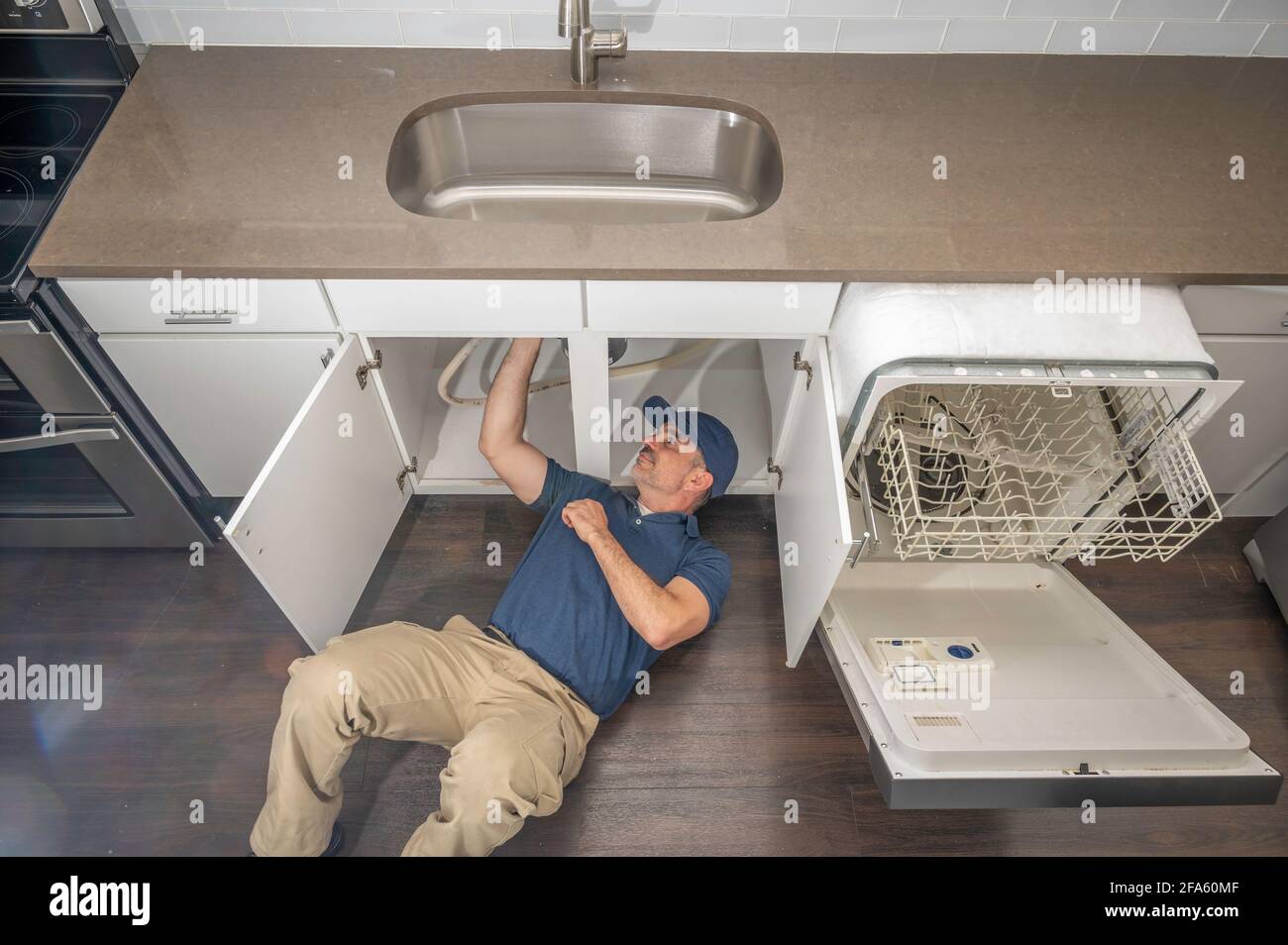 Gerätetechniker, der unter einem Spülbecken arbeitet und einen Geschirrspüler installiert Stockfoto